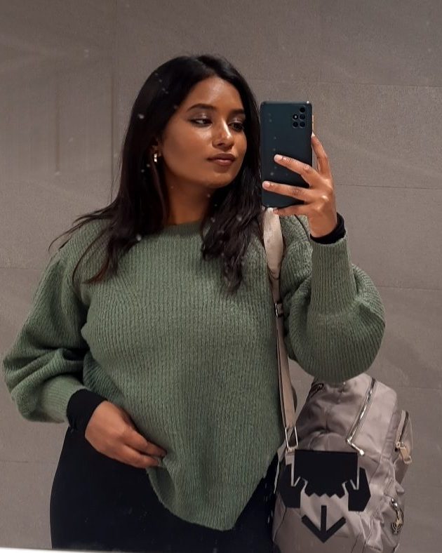 Charuta taking a mirror selfie in a green sweater